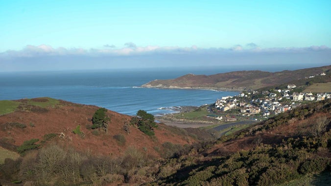 A scenic view of a small town by the ocean, captured from a hilltop, showcasing the coastline and surrounding landscape